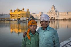 Two Young Boys Pose For A Photograph In Front Of The The Golden Temple , Amritsar At Dusk .