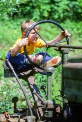 A Four Year Old Boy Sits Behind The Wheel Of An Antique Tractor Pretend Driving On The Farm In Ryegate , Vermont , United States .