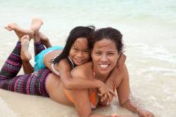 A Young Filipino Girl Lays On Her Mother’s Back On The Beach At Pandan Island, Puerto Princesa, Palawan Island, Philippines.