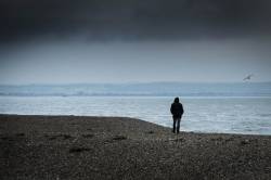 A Man Walking Along The Shingle Beach At Dungeness In Kent.