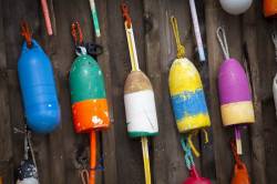 Five Colorful, Brightly Painted Bullet Nose Lobster Buoys, Also Called Floats, Hang On The Outside Wall Of A Rustic, Wooden Shed In Camden, Maine. Color Patterns Identify The Different Owners.