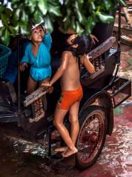 Two Young Cambodian Khmer Children Play In The Rain Catching Drops Shed By Tree Leaves In Siem Reap, Kingdom Of Cambodia.