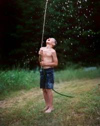 Elementary Age Boy Squirting Water Into The Air With A Garden Hose.