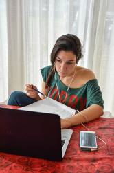 Young Female Student Listening To Her Cell Phone While Searching For Information On Her Laptop