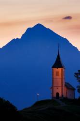 Jamnik Church Of Saints Primus And Felician At Sunrise, Perched On A Hill On The Jelovica Plateau With The Kamnik Alps And Storzic Mountain In The Background, Slovenia.