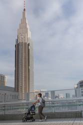 A Mother Pushes A Baby Stroller In Front Of The Docomo Tower In Shinjuku, Tokyo, Japan Friday June 9th 2017