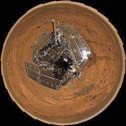 This Birds Eye View Combines A Self Portrait Of The Spacecraft Deck And A Panoramic Mosaic Of The Martian Surface As Viewed By NASAs Mars Exploration Rover Spirit The Rovers Solar Panels Are Still Gleaming In The Sunlight , Having Acquired Only A Thin Veneer Of Dust Two Years After The Rover Landed And Commenced Exploring The Red Planet Spirit Captured This 360 Degree Panorama On The Summit Of " Husband Hill " Inside Mars Gusev Crater During The Period From Spirits Martian Days , Or Sols , 583 To 586 ( August 24 To 27 , 2005 ) , The Rovers Panoramic Camera Acquired The Hundreds Of Individual Frames For This Largest Panorama Ever Photographed By Spirit This Image Is An Approximately True Color Rendering Using The Cameras 750 Nanometer , 530 Nanometer And 480 Nanometer Filters For The Martian Surface , And The 600 Nanometer , 530 Nanometer , And 480 Nanometer Filters For The Rover Deck This Polar Projection Is A Compromise Between A Cylindrical Projection Which Provides The Best View Of The Terrain , And A Vertical Projection , Which Provides The Best View Of The Deck But Distorts The Terrain Far From The Rover The View Is Presented With Geometric Seam Correction